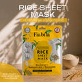 Fiabila Rice Sheet Mask packaging displayed on a wooden surface with a bowl of rice and wheat stalks, under warm natural light with leaf shadows. The packaging is bright yellow and white with illustrations of rice grains.