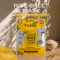 Fiabila Rice Sheet Mask packaging displayed on a wooden surface with a bowl of rice and wheat stalks, under warm natural light with leaf shadows. The packaging is bright yellow and white with illustrations of rice grains.