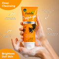 A hand holding a tube of Fiabila Papaya Face Wash with foam on the fingers, set against a warm beige background with promotional text overlays highlighting deep cleansing and brightening benefits.
