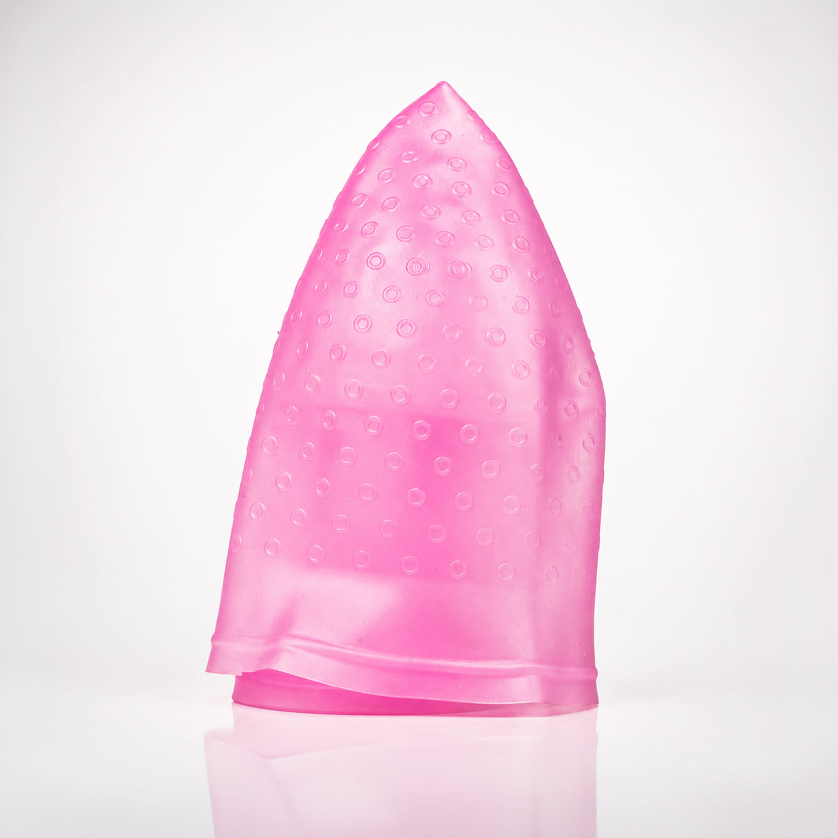 A translucent pink silicone hair cap with a textured bubble pattern, standing upright on a reflective white surface against a white background.